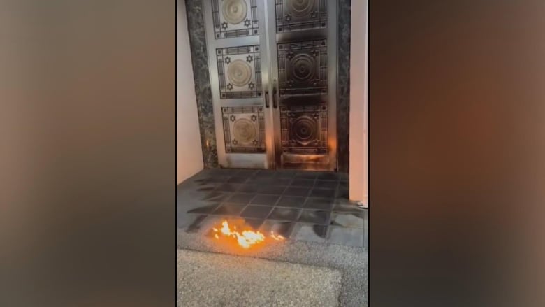 a fire burns on the ground outside of the front doors of a synogogue