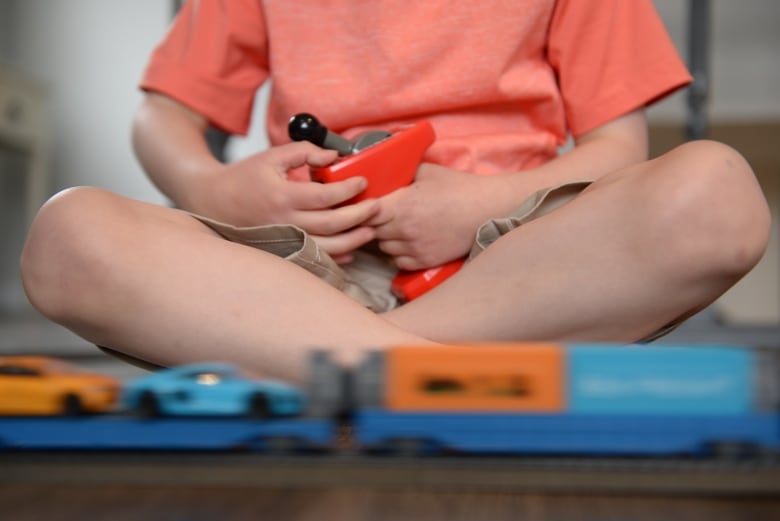 A boy wearing shorts and a t-shirt is photographed from the neck down playing with toy cars. 