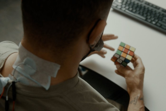 A person with an external device on his nape works on a Rubik’s Cube