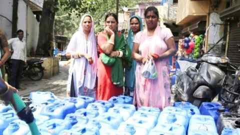 Four women wait as a man fills large cans with water