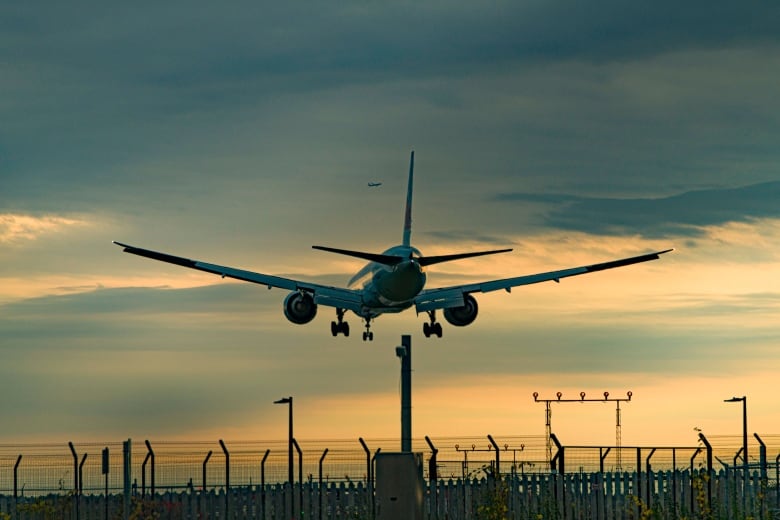 An airplane goes in for a landing at an airport. Another plane can be seen taking off in the distance.