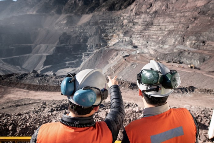 Two men in hard hats stand on edge of an open-air mine