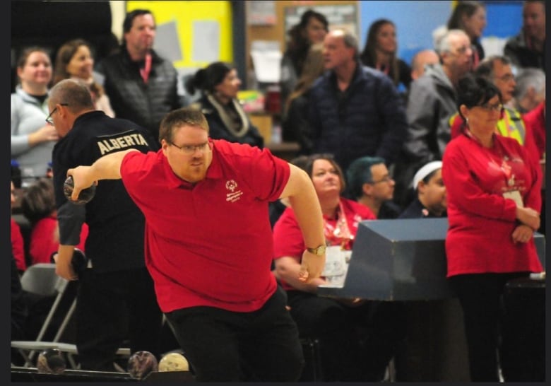 Man wearing a red shirt about to release a ball in 5-pin bowling at the Special Olympics. 