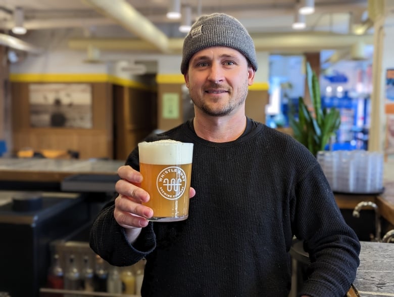 A man wearing a grey toque holds a glass of beer