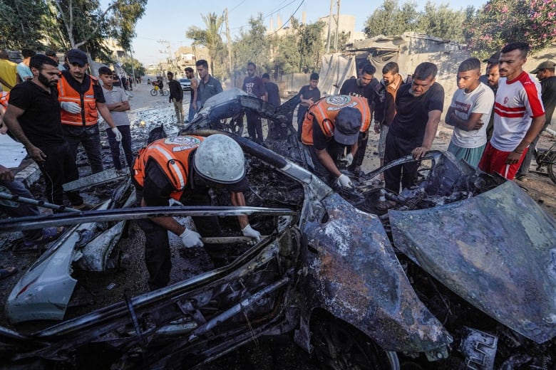 Several people, including workers in reflective vests, inspect large pieces of metallic-looking debris, seemingly from a vehicle.