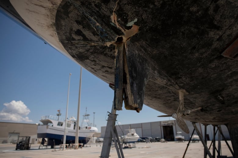 A boat is up on lifts, revealing a rudder that is cracked in several places and missing its bottom.