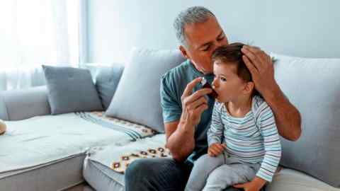 A caring father gives asthma medicine to his toddler son using an inhaler