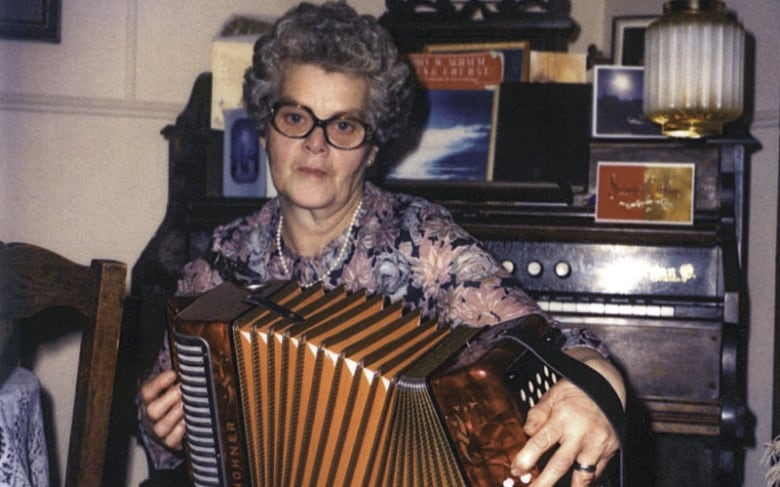 An older woman with glasses expands her accordion while playing it. 