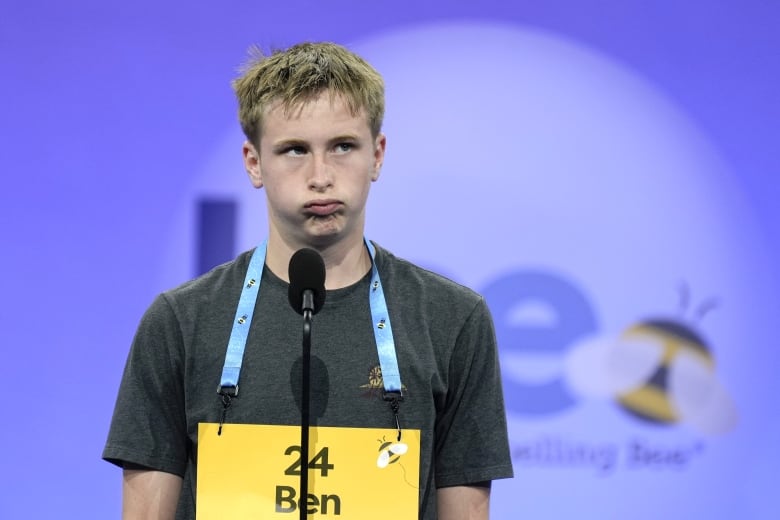 A young boy in dark t-shirt puffs out his cheeks during a spelling competition.