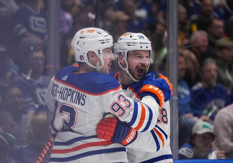 Two hockey players wearing white celebrate on the ice.