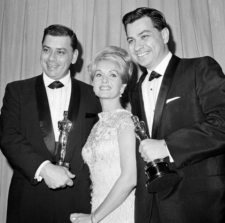 Three people pose for photos while holding awards in this black and white image.