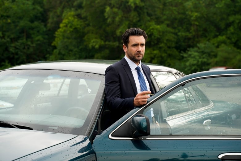 A man in a suit steps out of a car.