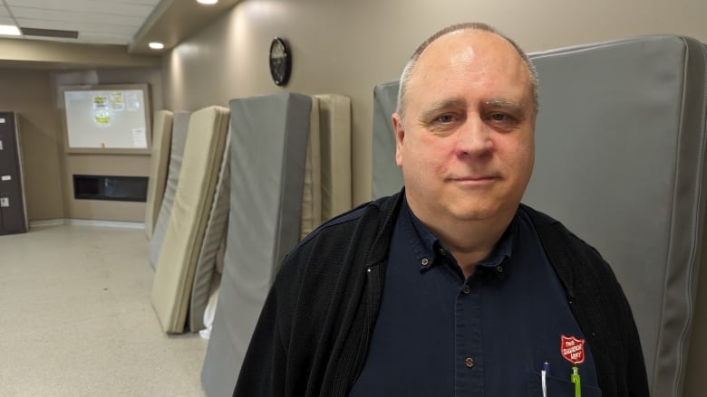 A man in a button up shirt and a sweater standing in front of cot beds