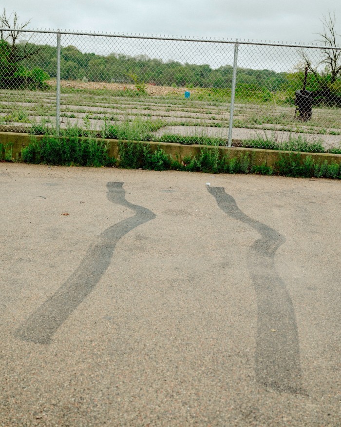 Tyre tracks lead up to a wire fence beyond which lies an expanse of concrete and weeds