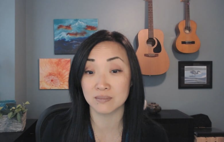 A woman sits in an indoor room with a paintings and a pair of guitars seen hanging on the wall behind her.