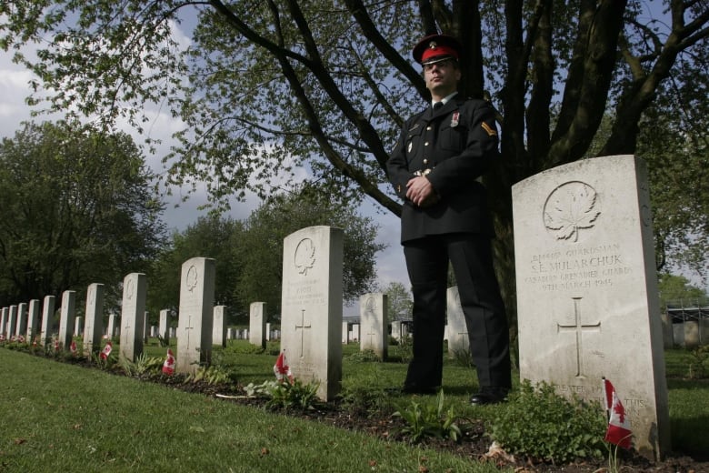 A man in uniform stands among gravestones in a cemetery.