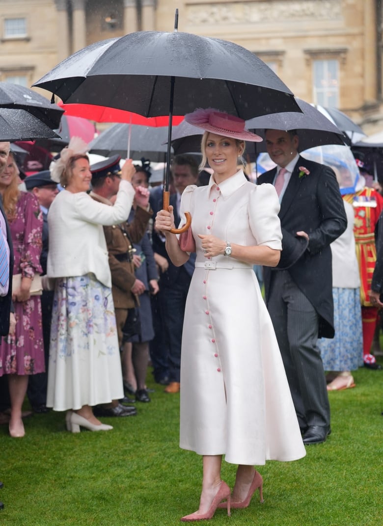 A person holding an umbrella stands in front of several other people holding umbrellas on a lawn in front of a stone building.