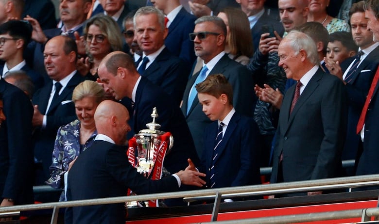 A man shakes a child's hand as other adults stand nearby. A large trophy is between them.