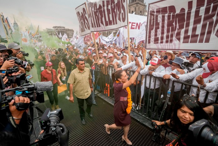 Sheinbaum waves to the banner-carrying crowds behind barriers