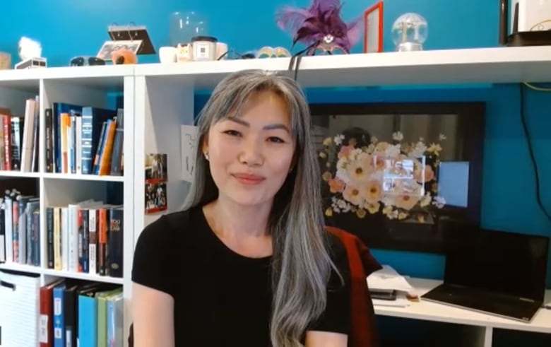 An East Asian woman with silber hair smiles in front of bookcase.