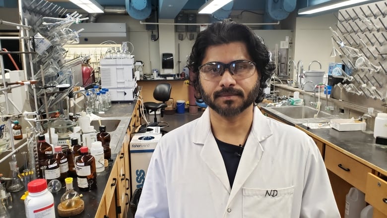 ABAzyne chemist Naveen Diddi stands for a photo in a white lab coat in a laboratory.