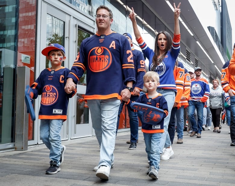 Adult and children wearing Edmonton Oilers jerseys walking on a sidewalk. 