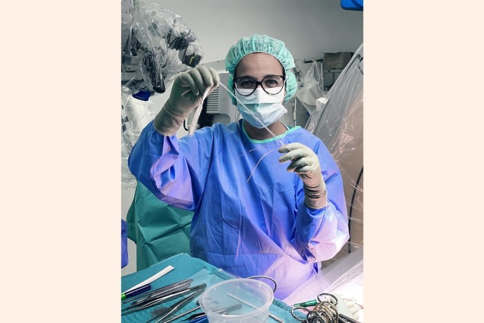 Jocelyne Bloch, wearing surgical scrubs, hat and facemask, holds up Onward’s first implant