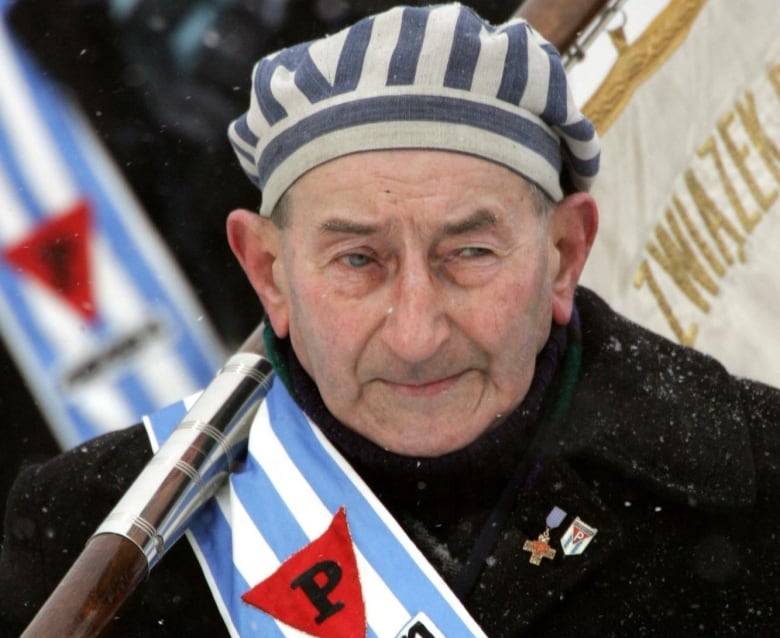 An old man  wears a striped sash with a red triangle on it