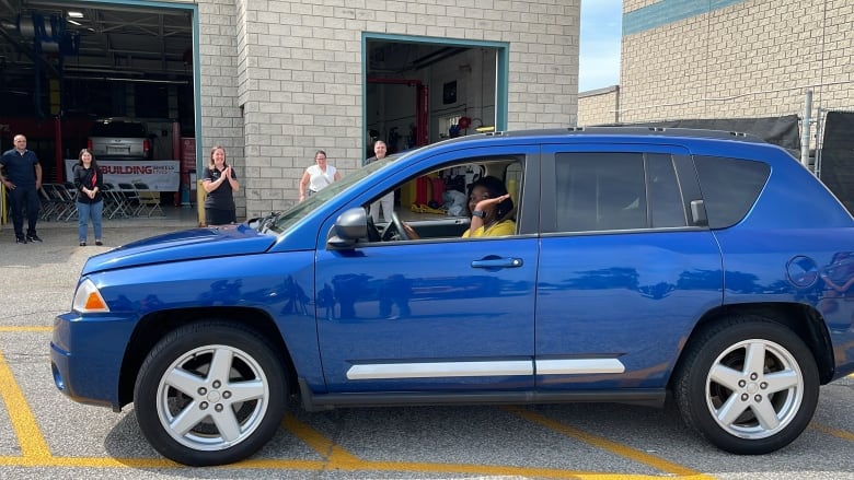 A woman smiles from the window of a bright blue car