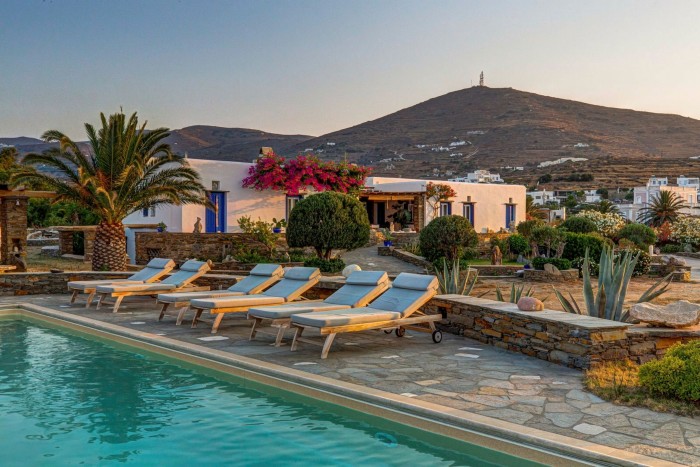 A poolside terrace and gardens with a blue and white villa in the background