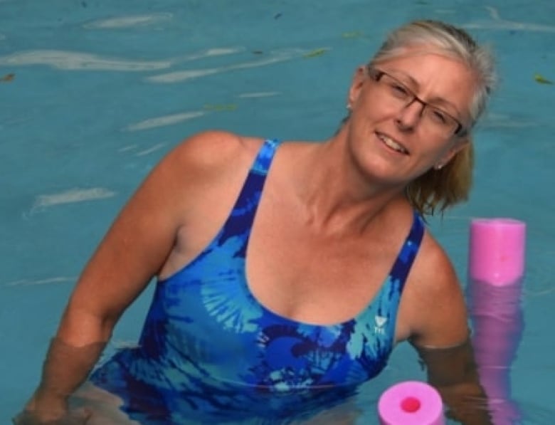 A woman in a swimming pool holds a pool noodle under the surface.