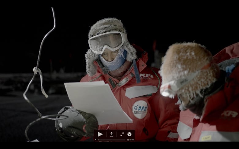 A woman outdoors in a cold, dark, Arctic environment studying a paper.