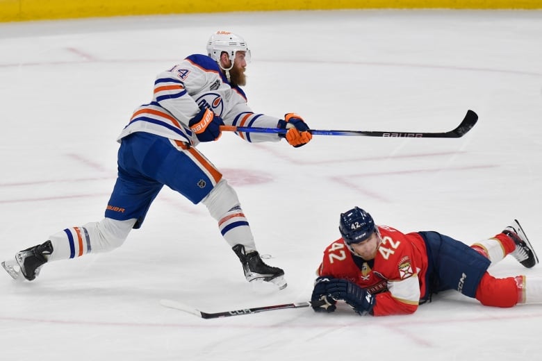 A hockey player shoots as an opposing player slides in an attempt to block.