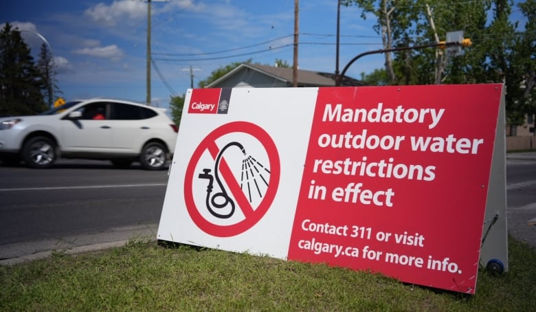 a sandwich board sign on green grass reads "mandatory outdoor water restrictions in effect"