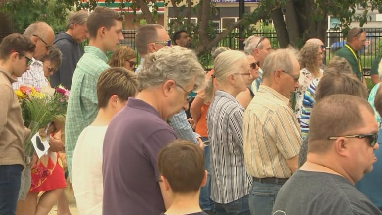 A group of people are pictured standing with their heads bowed.