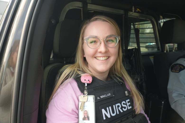 A woman sits in a the passenger seat of a police vehicle with a vest emblazoned with the word "nurse."