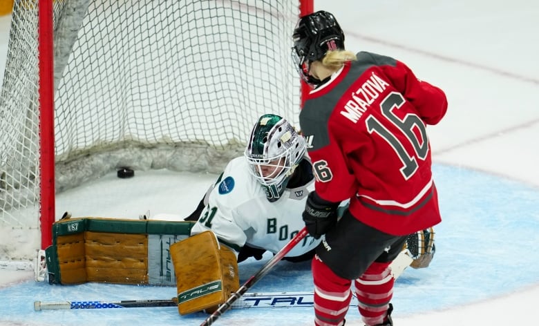 A women's hockey player scores a game-winning goal while the opposing goalie lays on the ice.