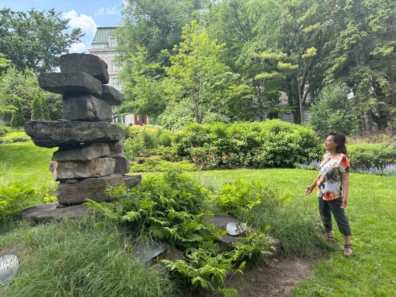 A woman stands looking up at an Inukshuk monument.