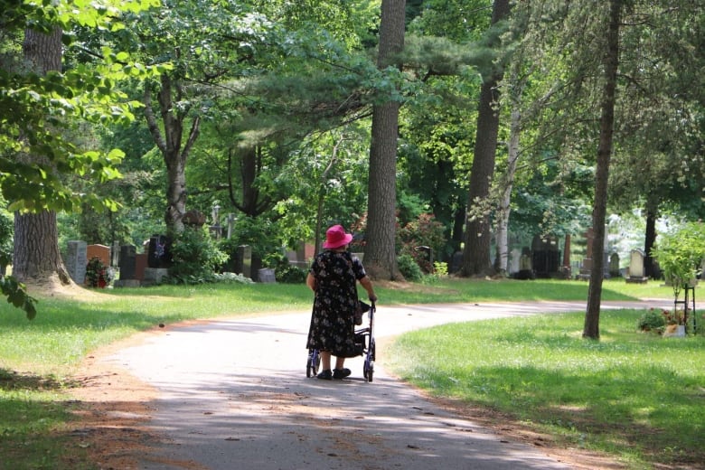 A woman with a cane walks along a path in a cemetery