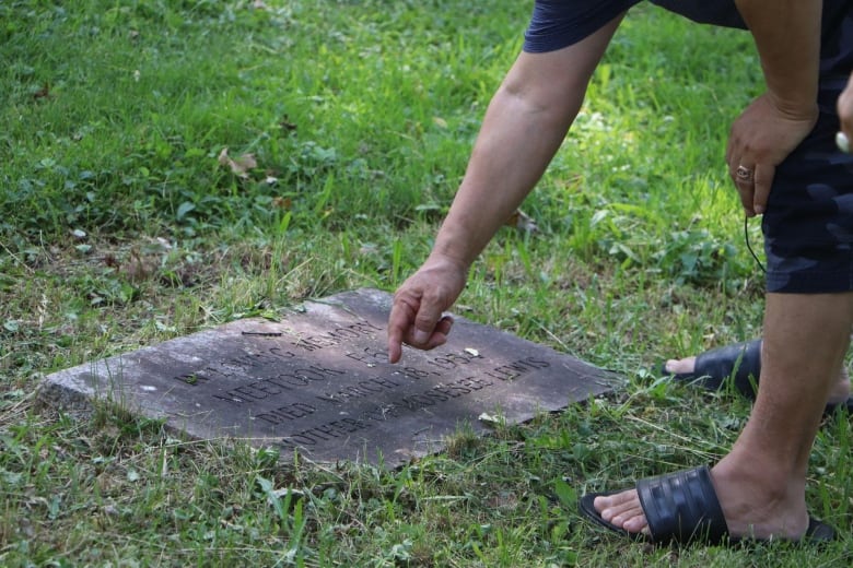 A man points to a grave in a graveyard