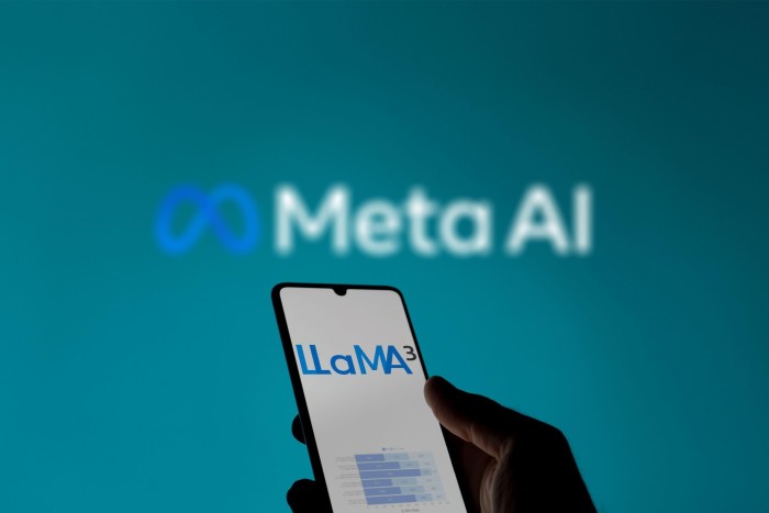 A hand holding a smartphone displaying the logo and text “LLaMA3” against a blurred background featuring the “Meta AI” logo