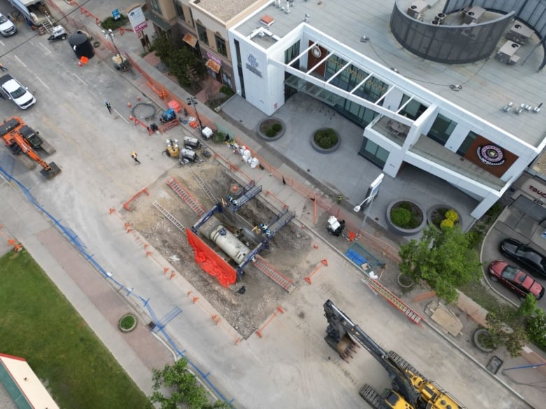 an aerial view of an open excavation showing a large pipe and multiple construction workers.