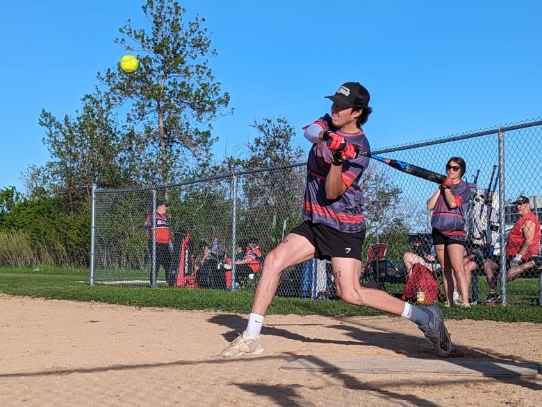 A man swings a bat at a softball on a baseball diamond.