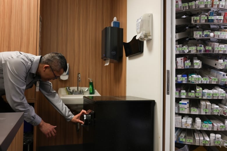 A man bends over to enter a combination on a time-delay safe in a pharmacy.