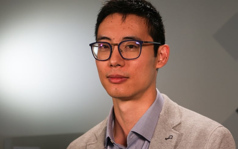 A man in a suit jacket and glasses looks at the camera.