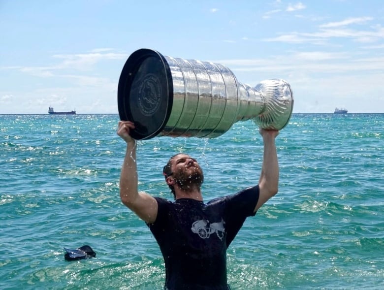 A man hoists a trophy in the air in the ocean