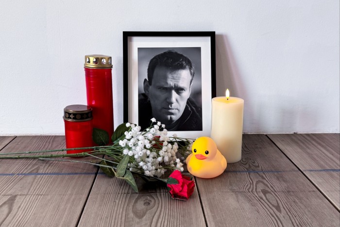 A black-and-white portrait of Alexei Navalny with flowers, candles and a rubber duck