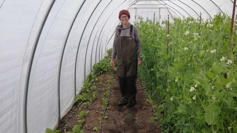 Woman wearing overalls stands beside a row of beets