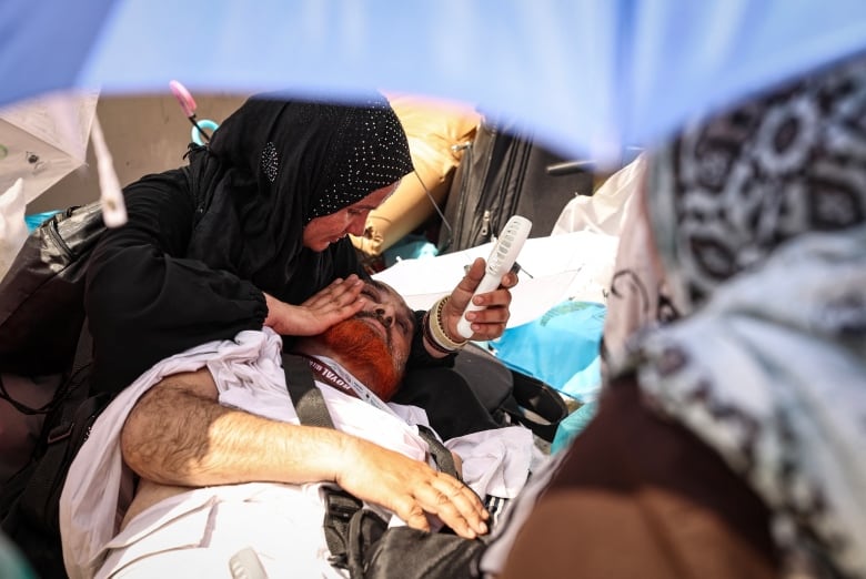 A woman uses a hand held battery run fan to cool off a man lying on the ground, affected by the scorching heat, during the symbolic 'stoning of the devil' ritual at the annual hajj pilgrimage in Mina on June 16, 2024. 