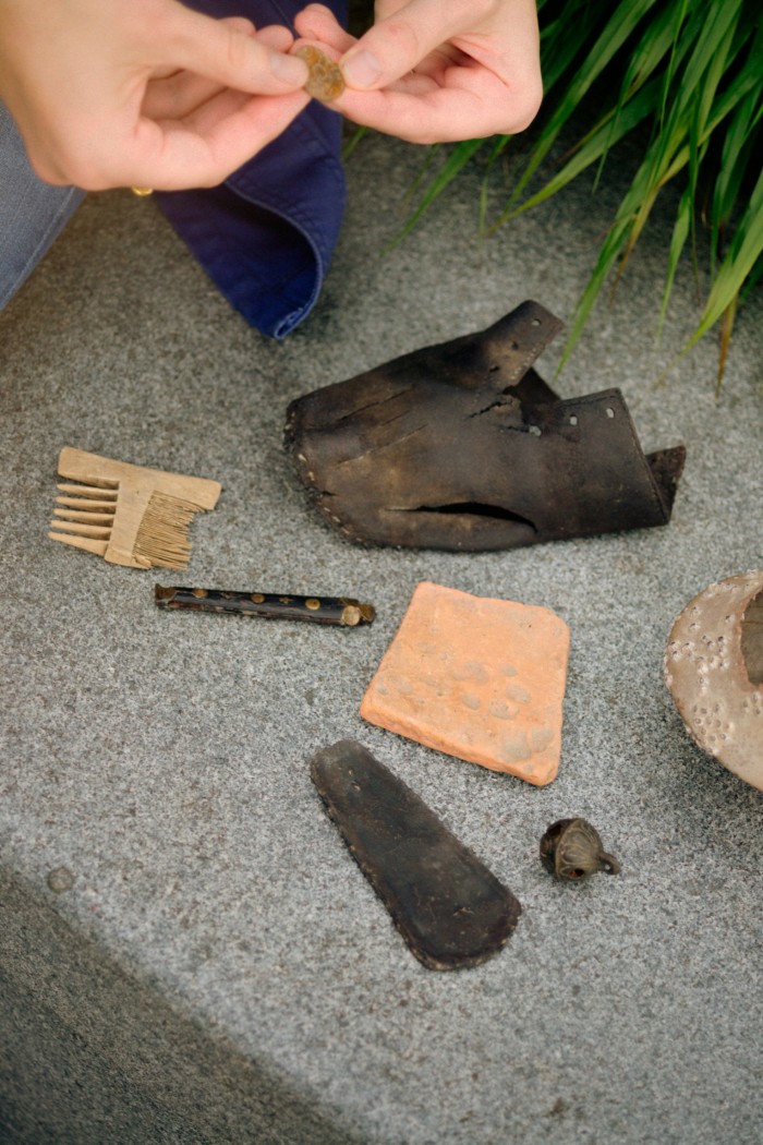 A pair of hands picks over fragments of ancient artefacts, including a comb and a leather shoe